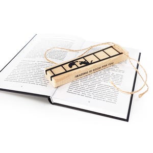 Metal cat bookmark with ladder design resting on an open book, packaged with a wooden block engraved “Reading is good for you” and natural twine.
