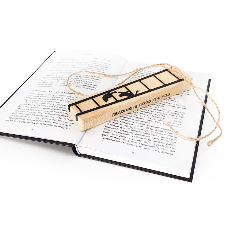Metal cat bookmark with ladder design resting on an open book, packaged with a wooden block engraved “Reading is good for you” and natural twine.
