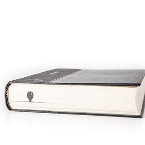Black metal bike bookmark peeking from the pages of a closed book, showing the balloon detail against the book’s edge on a white background.