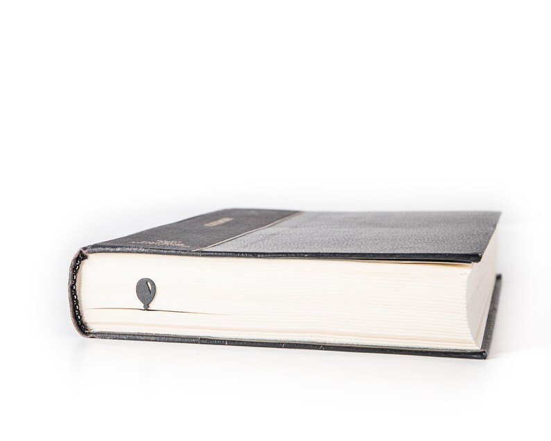 Black metal bike bookmark peeking from the pages of a closed book, showing the balloon detail against the book’s edge on a white background.