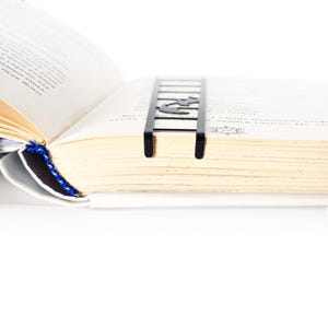 Black metal cat bookmark inserted between book pages, ladder design sitting flat and visible at the top of a thick open book.