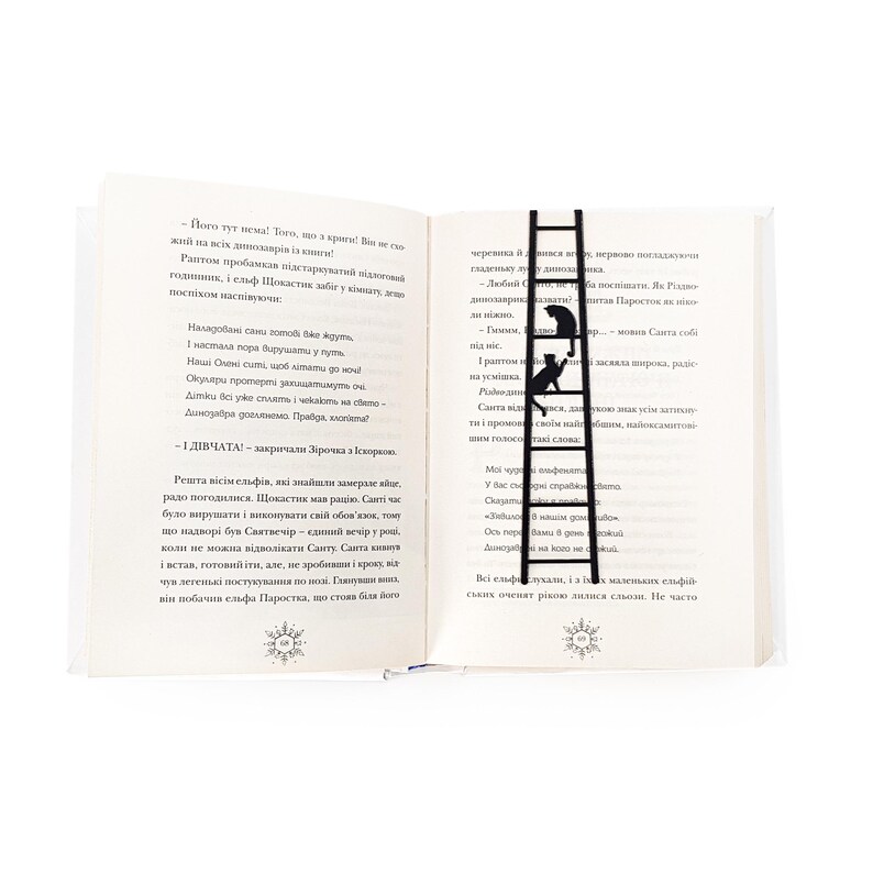 Black metal cat bookmark shaped like a ladder placed vertically between open book pages, with two cats climbing and visible above the text.