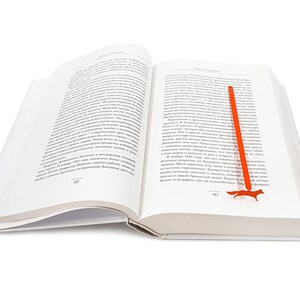 May include: An open book with a red fox bookmark. The book is open to page 333 on the left and 333 on the right. The bookmark is shaped like a fox and is made of metal.