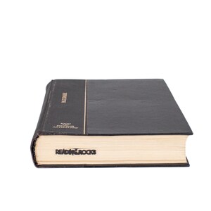 Black metal page saver with the phrase ‘READING ROCKS’ peeking from a closed hardcover book. A fun and bold gift for book lovers.