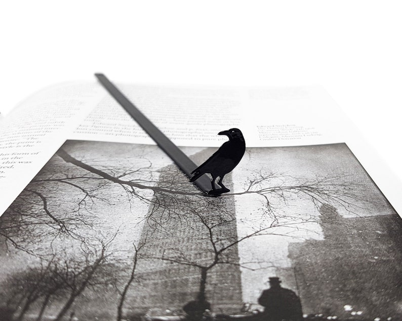 Black metal page saver shaped like a raven, perched on a grayscale photo of a foggy cityscape. A dark, poetic accessory for lovers of gothic fiction and urban mystery.