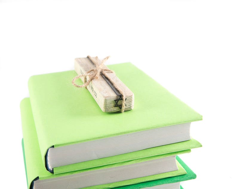 A stack of three green books with a David Star bookmark on the wooden block tied with twine. The bookmark is made by an indy shop in Ukraine. Not mass-manufactured.
