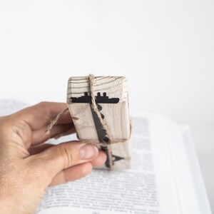 May include: A wooden bookmark with a black ship silhouette design. The bookmark is tied with twine and is being held by a hand.