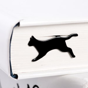 Laser-cut black metal bookmark Running Cat. A flat metal stick sits between the pages of the book. The running cat is seen on the side of the book even when its closed. Handcrafted in Cherkasy, Ukraine. Not mass-produced.