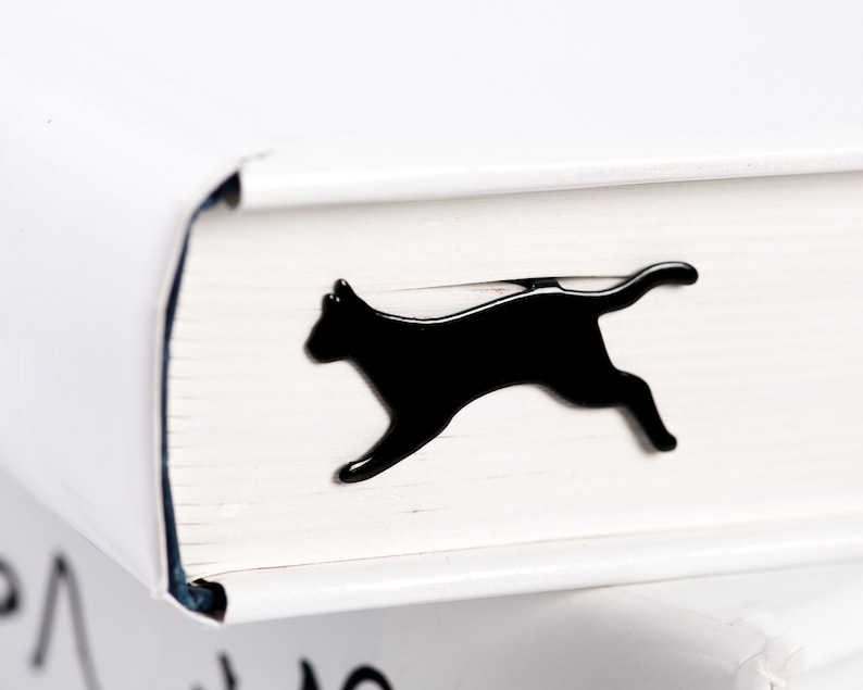 Laser-cut black metal bookmark Running Cat. A flat metal stick sits between the pages of the book. The running cat is seen on the side of the book even when its closed. Handcrafted in Cherkasy, Ukraine. Not mass-produced.