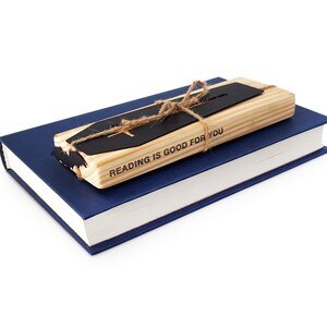 Black metal coffin-shaped bookmark with a wooden engraved block tied together with twine, resting on top of a closed blue hardcover book on a white background.