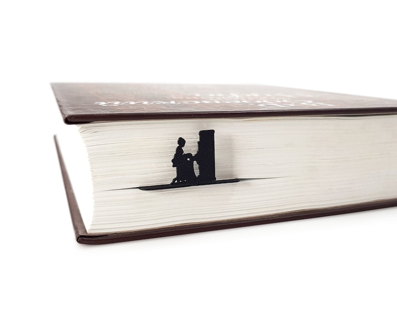 A black metal bookmark shaped like a person standing next to a building. The bookmark is placed on top of a closed book with a brown cover.