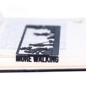 May include: Black metal bookmark with a cut-out design of trees and the words "MORE WALKING".