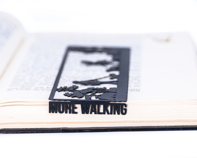 May include: Black metal bookmark with a cut-out design of trees and the words "MORE WALKING".