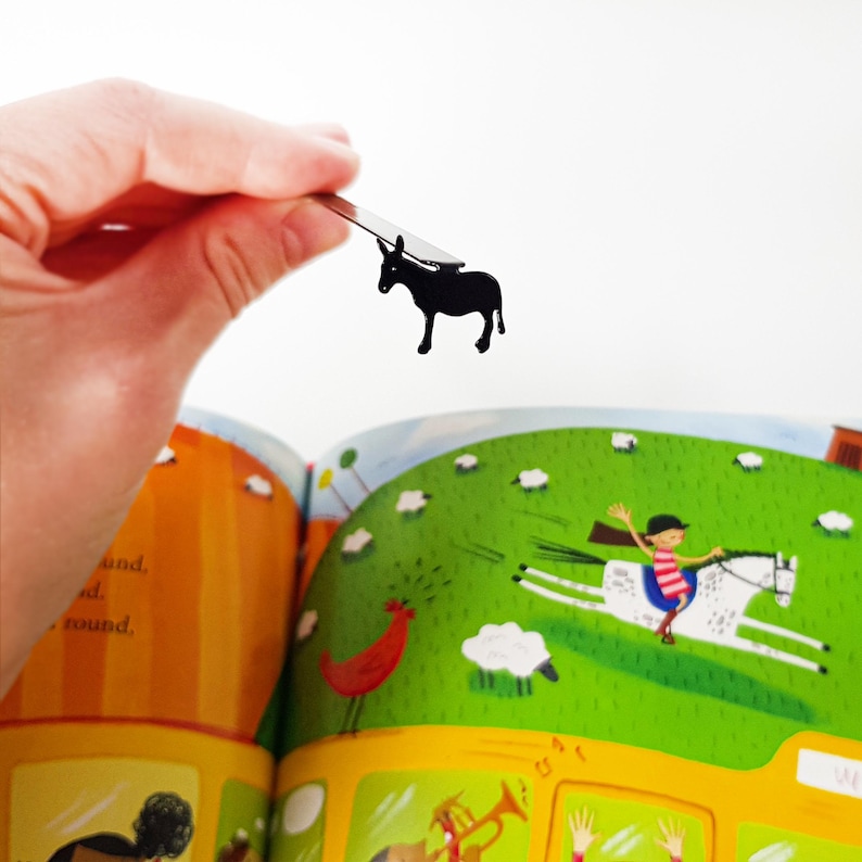 Hand holding black metal donkey bookmark above open children's farm book