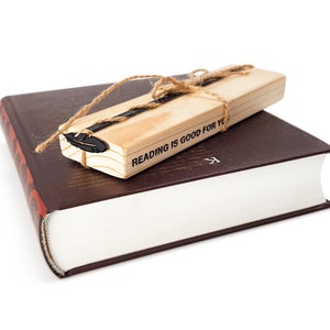 May include: A brown hardcover book with a wooden bookmark. The bookmark is tied with twine and has a feather design. The bookmark has the text "Reading is good for you".