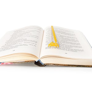 May include: A yellow metal bookmark shaped like a spaceship is placed in an open book. The book is open to page 119.
