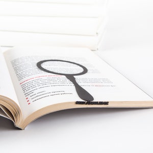 Black metal bookmark Magnifying Glass in the book. The writing on the side says Seek Knowledge.