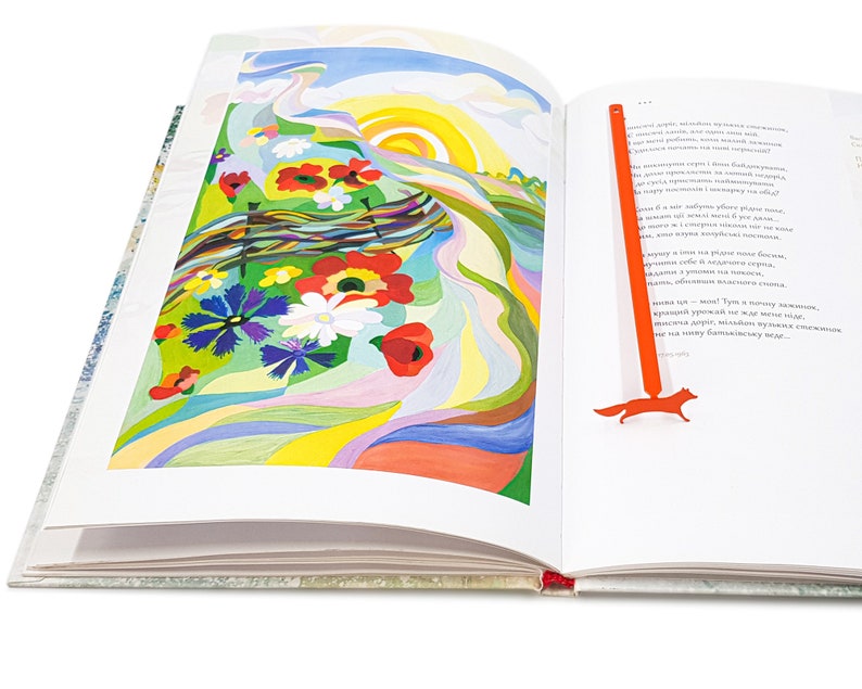 May include: An open book with a colorful illustration of a field of flowers and a bright sun. A red fox bookmark is on the right page.