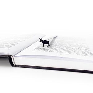 Black donkey metal bookmark on open book lying on white surface