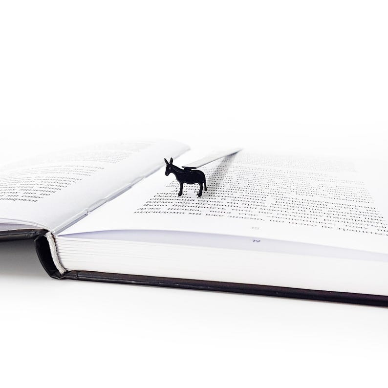 Black donkey metal bookmark on open book lying on white surface