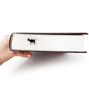 Hand holding closed hardback book from spine with black donkey metal bookmark