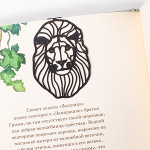 May include: Black paper cut-out of a lion's head with a detailed mane. The lion's head is facing forward with a serious expression. The cut-out is on a white background.