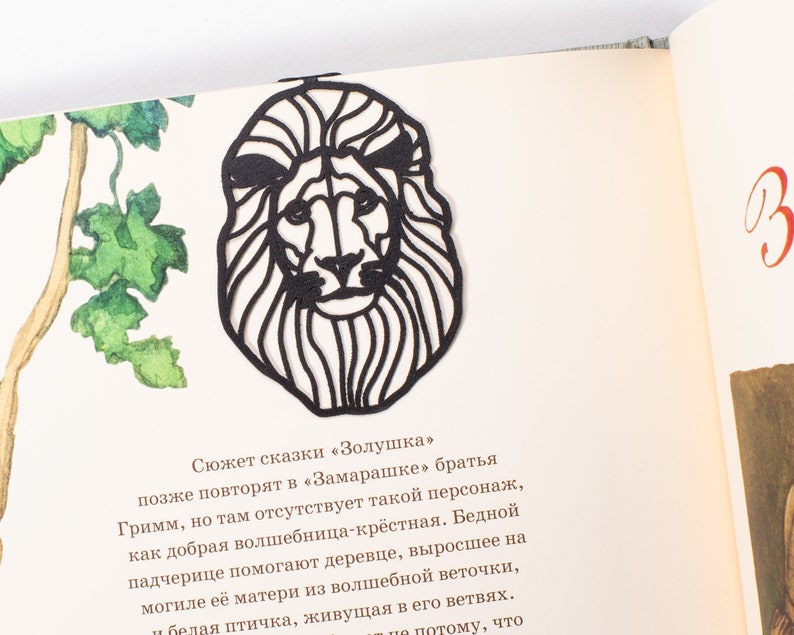 May include: Black paper cut-out of a lion's head with a detailed mane. The lion's head is facing forward with a serious expression. The cut-out is on a white background.