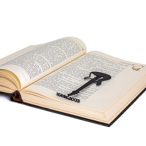 Black metal bookmark Reading Rocks. The cut out of metal silhuette of the guitear is sitting between the pages of the book. The writing Reading Roack is seen on the side of the book even when the book is closed. Designed and made by Coolbookmark on Etsy.