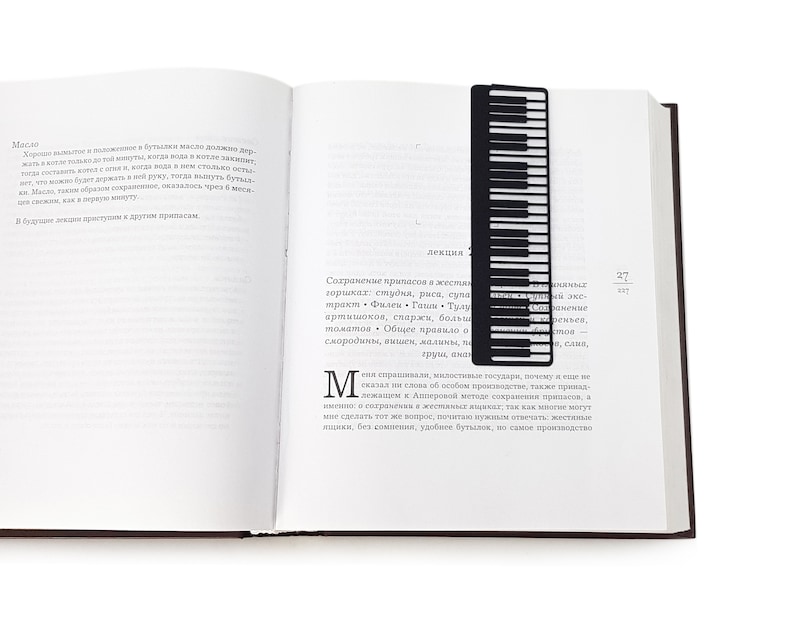 Black metal bookmark Piano Player. The line of piano keys stays between the pages of the book. A silhouette of the lady in a long dress playing the piano stays on the side of the book even when the book is closed. Made by us in our workshop.