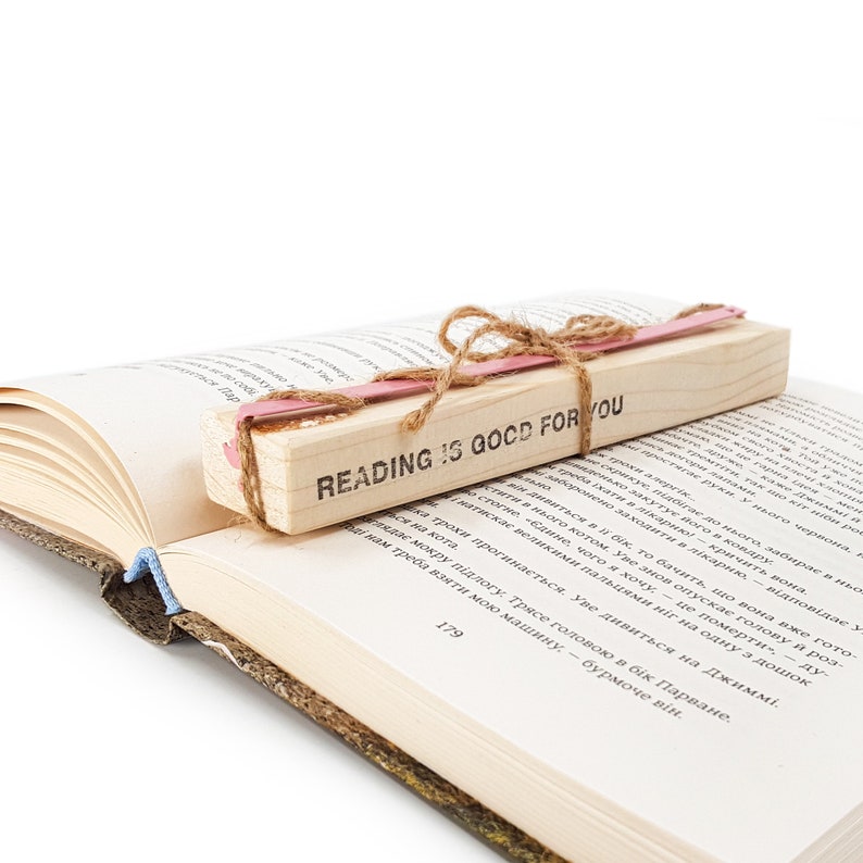 Pink metal bookmark Flamingo on the wooden block. A long, flat metal stick stays between the pages of the book - Cool Bookmark