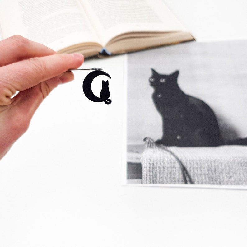 May include: Black metal bookmark featuring a crescent moon with a cat silhouette sitting on top.