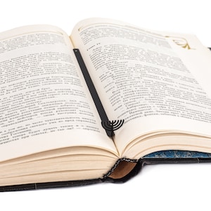 Black metal bookmark shaped like a menorah, resting neatly between the pages of an open book. A meaningful gift for Jewish readers and Hanukkah celebrations.