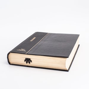 May include: A black hardback book with gold lettering on the spine that reads "LECTURES" and "WOOD FROM THE ANTILLES". The book has a black bookmark with a leaf design.