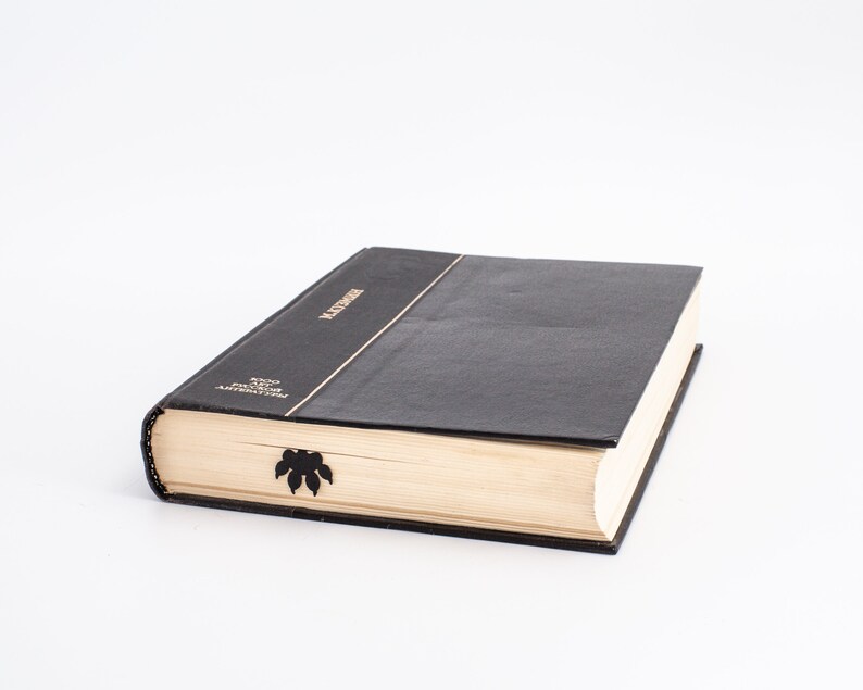 May include: A black hardback book with gold lettering on the spine that reads "LECTURES" and "WOOD FROM THE ANTILLES". The book has a black bookmark with a leaf design.