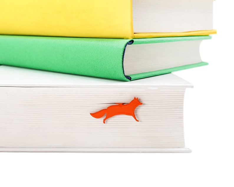 May include: A stack of three books with a white cover, a green cover, and a yellow cover. A red fox bookmark is sticking out of the top book.