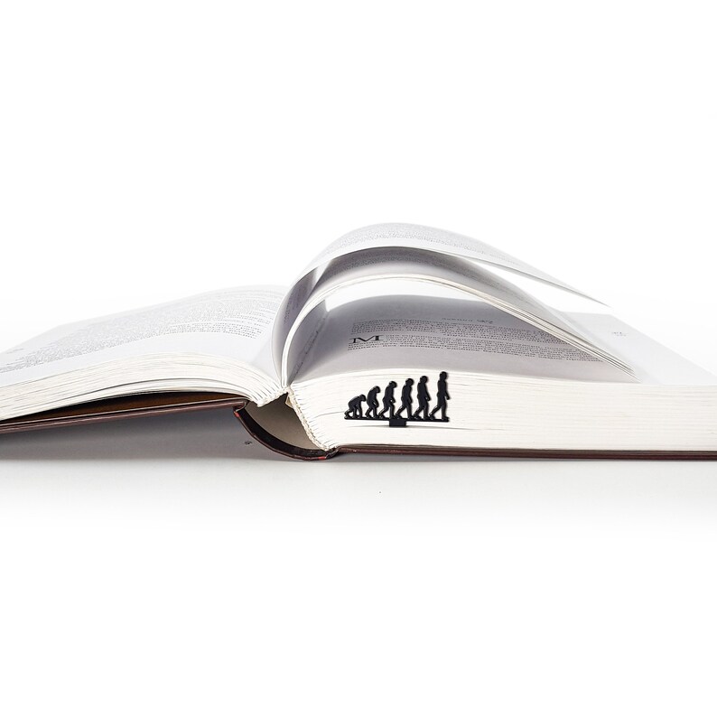 May include: A black metal bookmark shaped like the evolution of humans, from ape to modern human, is placed in an open book.