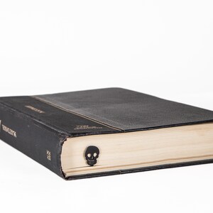 May include: A black hardcover book with a skull bookmark. The book has a gold title on the spine.
