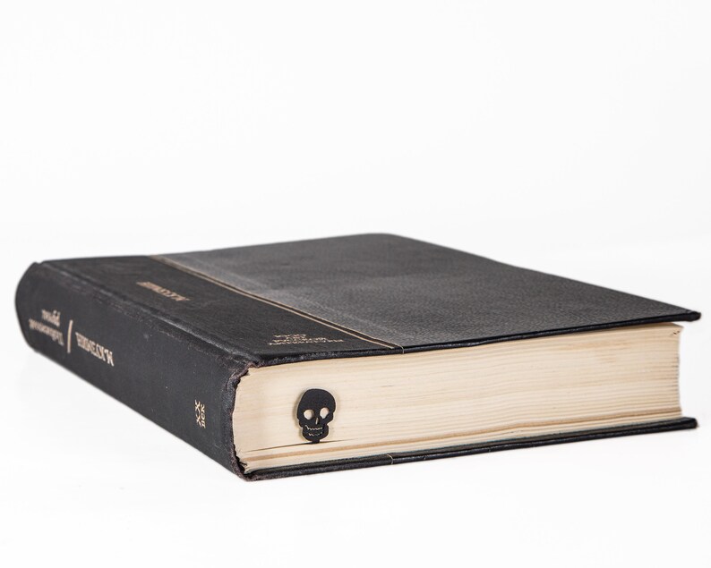 May include: A black hardcover book with a skull bookmark. The book has a gold title on the spine.