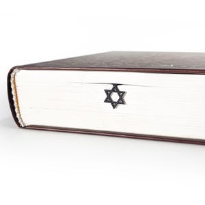 Black Star of David metal bookmark inserted in a closed thick book with brown cover, minimal Judaica gift idea for readers and scholars.