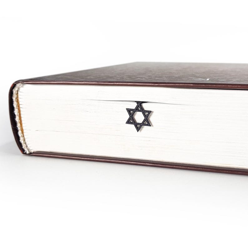 Black Star of David metal bookmark inserted in a closed thick book with brown cover, minimal Judaica gift idea for readers and scholars.