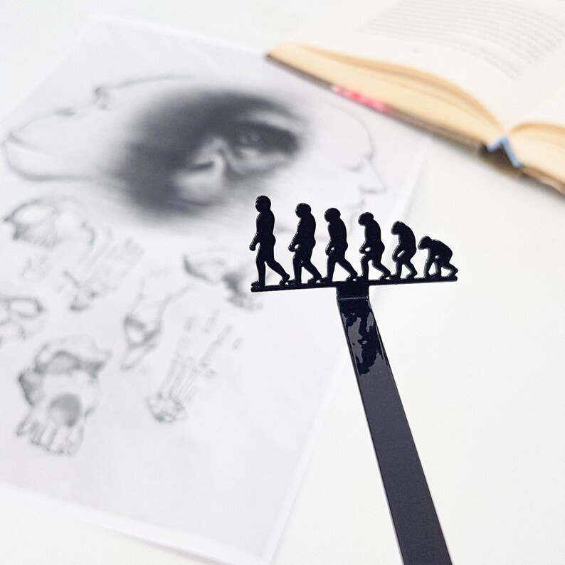 May include: A black metal bookmark shaped like a line of figures representing the evolution of humans. The figures are in silhouette and are walking in a line from left to right.
