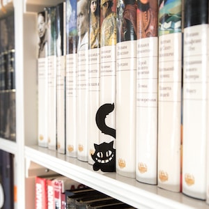 Black metal bookmark Cheshire Cat. The cat is visible on the shelf when the book divider is put in between the books - Coolbookmark.