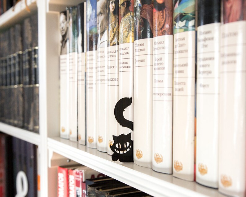 Black metal bookmark Cheshire Cat. The cat is visible on the shelf when the book divider is put in between the books - Coolbookmark.