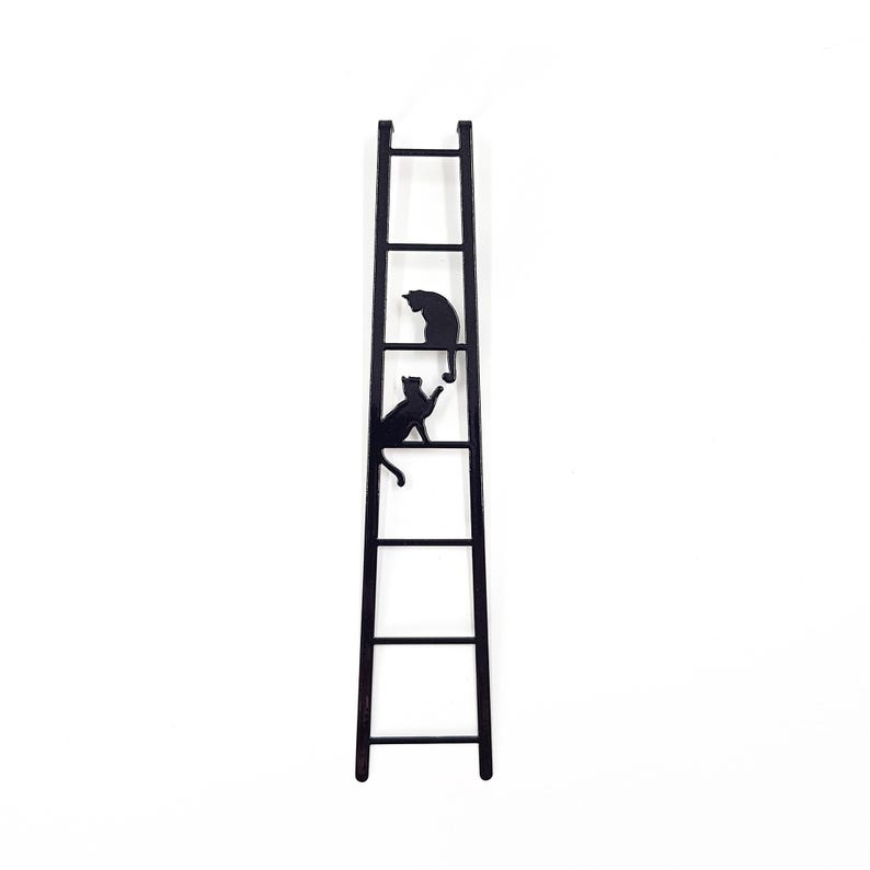 Black metal bookmark shaped like a ladder with two cats climbing, minimalist silhouette design on a white background.