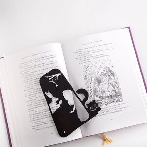 Black metal bookmark Cheshire Cat. The cat is visible on the shelf when the book divider is put in between the books - Coolbookmark.