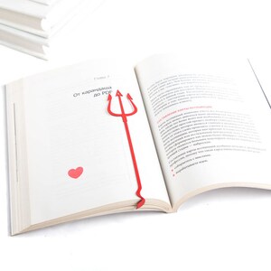 May include: A red plastic bookmark shaped like a trident with a small red heart on the page. The bookmark is in an open book with the text "От карандаша до PDF" on the page.
