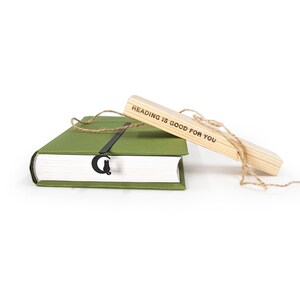 May include: A green book with a black bookmark shaped like a cat and a crescent moon. A wooden bookmark with the text "Reading is good for you" is resting on top of the book.