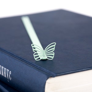 May include: A blue hardcover book with a light green butterfly bookmark. The book title is "The Genius" in white lettering.
