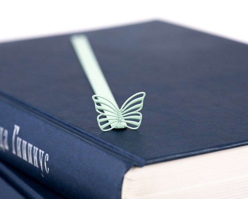 May include: A blue hardcover book with a light green butterfly bookmark. The book title is "The Genius" in white lettering.