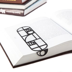 A black metal bookmark Bauhaus in the shape of a geometric design. The bookmark is placed in a book with white pages. Not mass-produced.